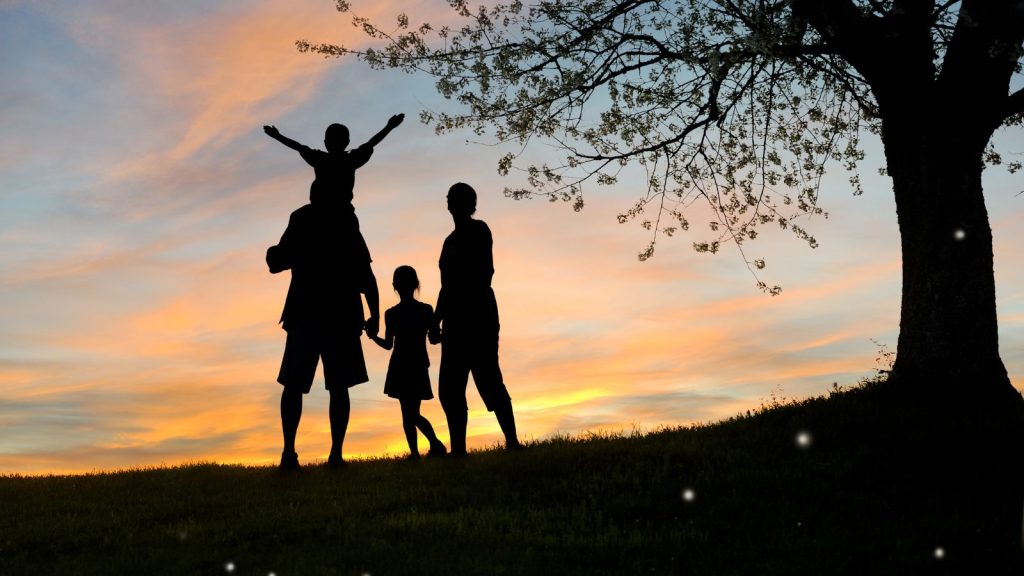Silhouette di una famiglia con due bambini al tramonto sotto un albero, a rappresentare le dinamiche relazionali e la base sicura trattate nell'articolo del blog di Polistudio Arcaro